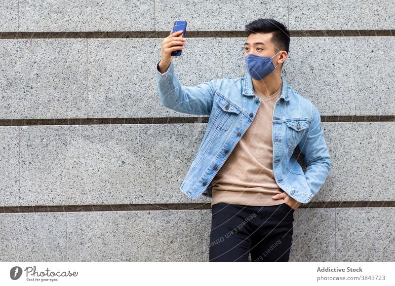 Ethnischer Mann in Maske nimmt Selfie in der Stadt Mundschutz Großstadt Smartphone Coronavirus Bund 19 Selbstportrait Pandemie Straße männlich ethnisch