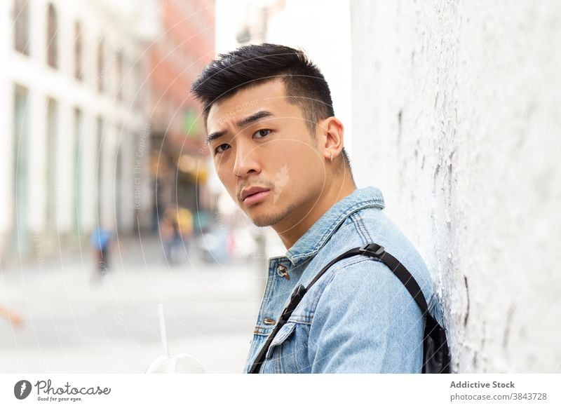Junger ethnischer Mann stehend auf der Stadtstraße urban jung asiatisch ernst Straße Hipster modern Schüler lässig männlich Großstadt Jeansstoff Stil
