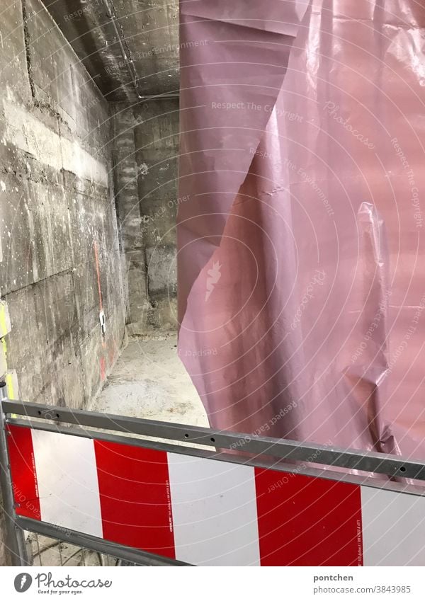 Eine lila Plastikplane hängt hinter einem Schrankenzaun vor einer betonmauer. Baustelle, Sicherheit Plane plastik baustelle schranke absperrung schrankenzaun