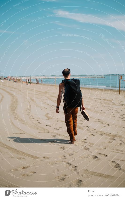 Ein Mann mit Rucksack spaziert im Urlaub einen Strand entlang und betrachtet das Meer. spazieren reisen Reisender Sandstrand Ferien & Urlaub & Reisen Mensch