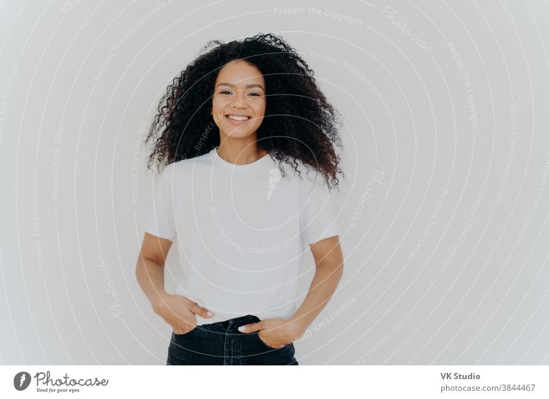 Einzelaufnahme einer jungen Afroamerikanerin in weißem T-Shirt, drückt gute Gefühle aus, steht allein im Haus, posiert für ein Foto, unterhält sich zwanglos mit einem Freund, genießt die Freizeit. Menschen und Glück