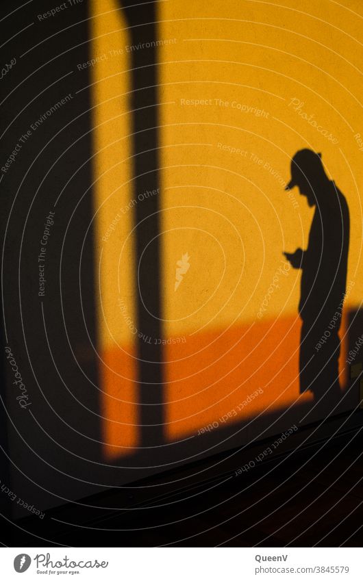 Schatten eines Mannes mit Handy Kommunikation orange Wand Telefon Lifestyle Mobile Technik & Technologie Internet modern Jugendliche Baseballmütze Gerät