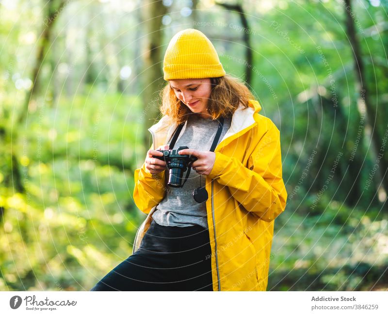 Fröhliche Frau mit Fotokamera im Wald Fotograf Reisender gelb Regenmantel Urlaub erkunden stehen genießen heiter Tourist Feiertag reisen Lächeln Fernweh