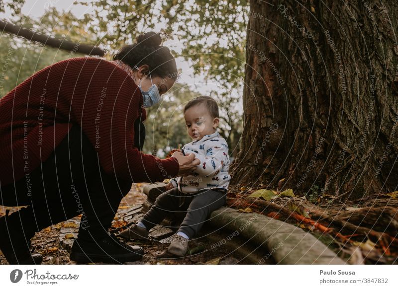 Mutter mit Maske und Kleinkind im Park 0-09 Jahre 30-39 Jahre anhänglich authentisch Herbst fürsorglich lässig Kaukasier Kind Farbe krause Haare Tag Genuss