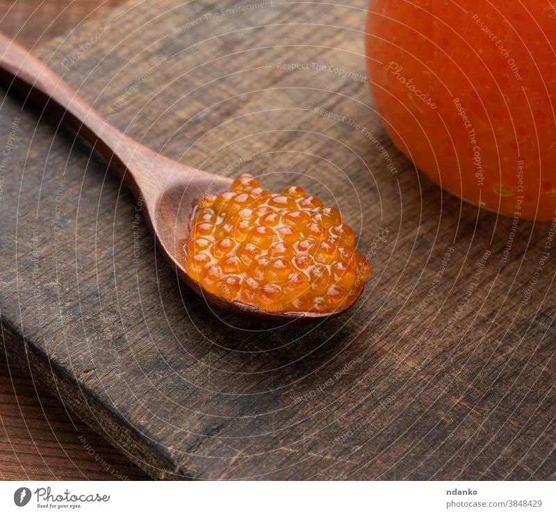 roter Kaviar in einem braunen Holzlöffel auf dem Tisch, hinter einem vollen Kaviarglas Lebensmittel Meeresfrüchte Fisch Löffel Reichtum rosa Lachs Feinschmecker