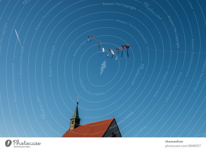 chinesische Drachen vor blauem Himmel über einer Kirche,  Kondensstreifen eines Flugzeugs Herbst Freiheit Schönes Wetter Windspiel