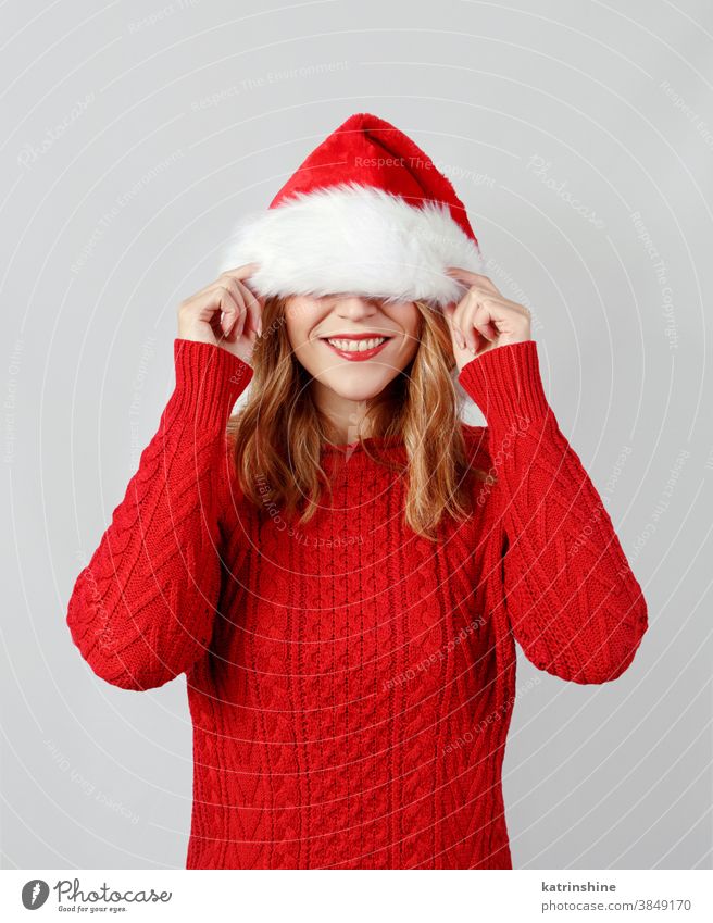 Junge Frau bedeckt ihre Augen, während sie den Weihnachtsmannhut berührt jung Hut Hände Geschenkverpackung Weihnachten Deckung präsentieren Lächeln weiß