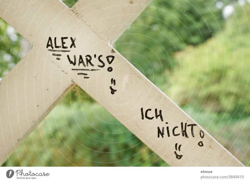 Im Park ist auf einer weißen Holzlatte mit schwarz in Druckschrift geschrieben: ALEX WAR's ! ICH NICHT ! Schrift Mitteilung Alex war's ich nicht verpetzen