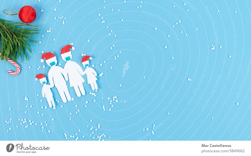 Aus Papier ausgeschnittene Familie mit Maske und Weihnachtshut auf blauem Hintergrund. Platz zum Kopieren. Blauer Hintergrund Weihnachten