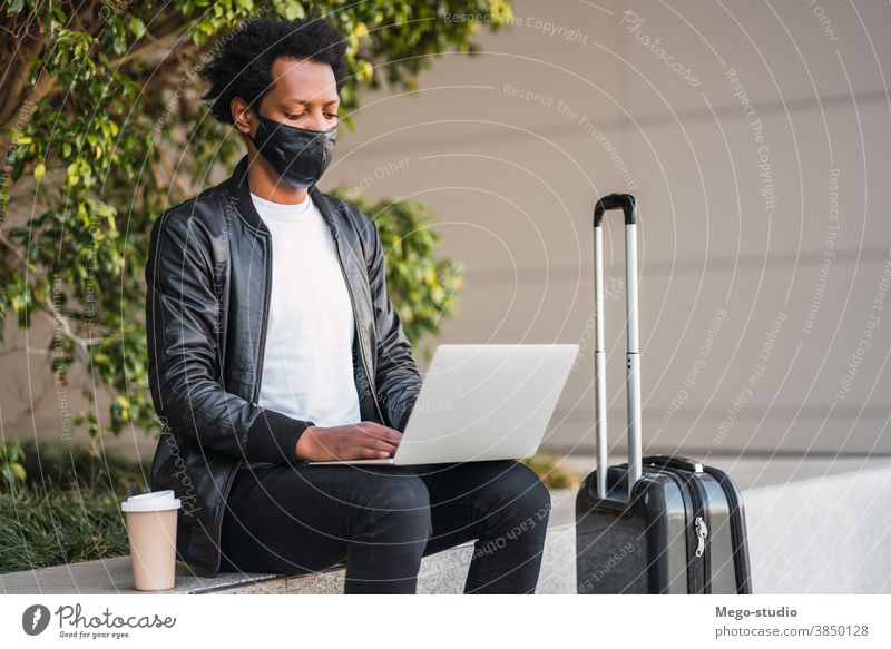Afrotourist, der seinen Laptop im Freien benutzt. Afro-Look Tourist Mann reisen Schutzmaske Porträt lässig Anschluss Feiertag Tourismus Virus Mundschutz