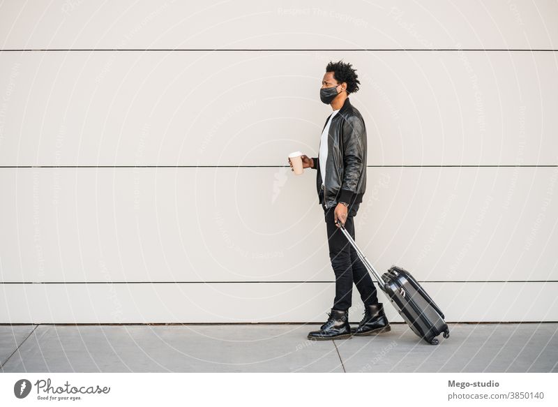 Tourist, der beim Spaziergang im Freien einen Koffer trägt. Afro-Look Mann Reisender Ausflugsziel Konzept Feiertag Tag Freude genießen Abenteuer Ferien Porträt
