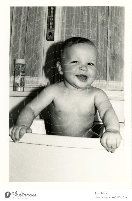 Ein kleiner Junge beim Baden in einer Kunststoffbadewanne hält sich am Rand fest und lächelt breit in die Kamera Baby Kleinkind 1-3 Jahre lächeln Freude sauber