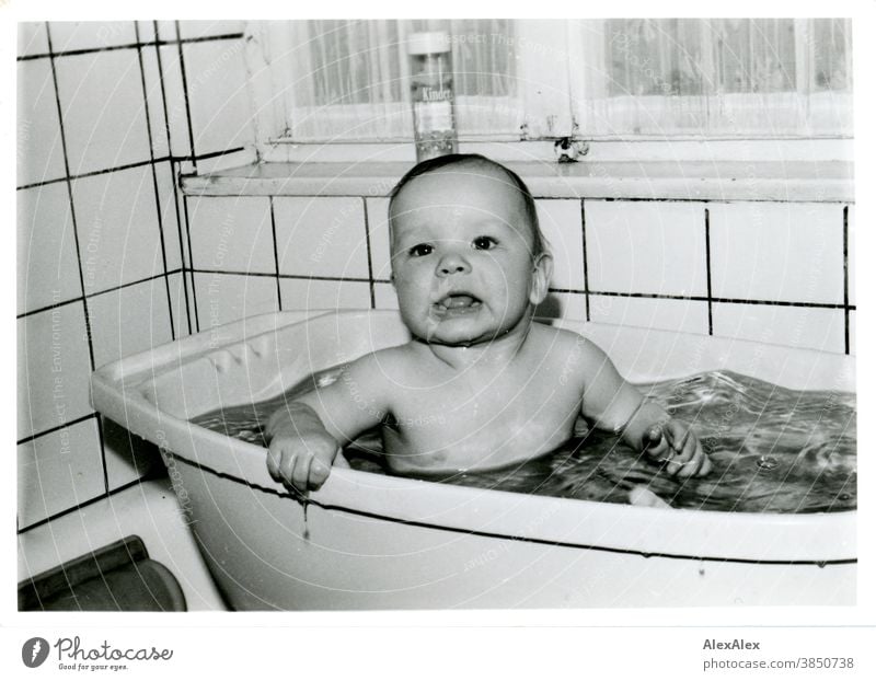 Ein kleiner Junge beim Baden in einer Kunststoffbadewanne hält sich am Rand fest und schaut in die Kamera Baby Kleinkind 1-3 Jahre sauber gewaschen Kind Mensch