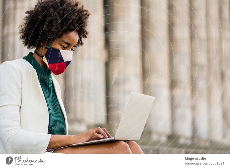 Geschäftsfrau, die ihren Laptop im Freien benutzt. jung Afro-Look Business Frau urban Straße Erfolg Gerät Gesichtsmaske Information behüten Schutzmaske covid-19