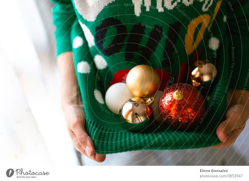 Unerkennbare Frau hält Christbaumkugeln in einem Weihnachtspullover mit Lichtern Weihnachten Frohe Weihnachten Neujahr Bälle Dezember Weihnachtskugeln Frauen