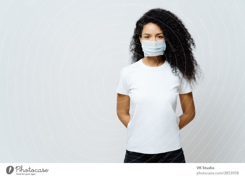 Halbe Aufnahme einer Afroamerikanerin, die sich in Selbstisolierung oder Quarantäne befindet, trägt während des Coronavirus-Ausbruchs eine medizinische Maske, hört Nachrichten, versucht, das Virus nicht zu verbreiten, bleibt lange zu Hause