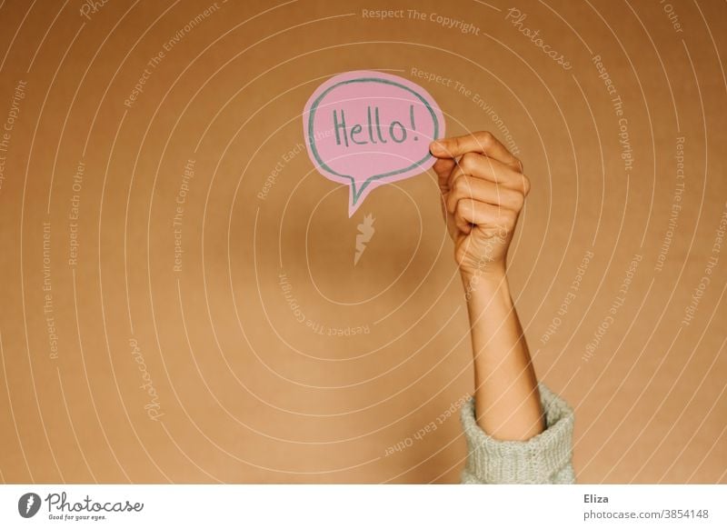 Hand hält eine Sprechblase in der Hello! steht. Grüßen auf Englisch. Hallo Fremdsprache kommunizieren Sprache Kommunikation Hi geschrieben Text braun lila