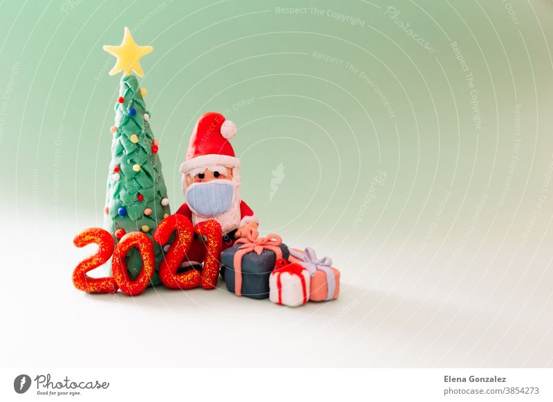 Verspieltes Ton-Weihnachtskonzept. Bunte, handgemachte Miniatur-Weihnachtsbäume, Geschenke und Weihnachtsmann mit Maske auf grünem Hintergrund. Neujahr 2021.