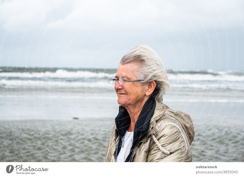 Senior Caucasian Woman Walking on Beach Profilansicht Frau Kaukasier Strand mittlere Aufnahme älter Porträt reales Leben bedeckt wolkig echte Menschen im Freien