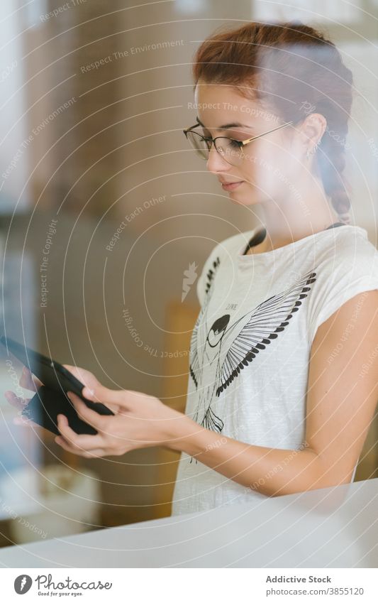 Junge Frau mit Tablette in der Nähe von Fenster benutzend Raum klug Fokus Daten lässig jung online konzentriert Brille Internet modern Gerät Apparatur Browsen