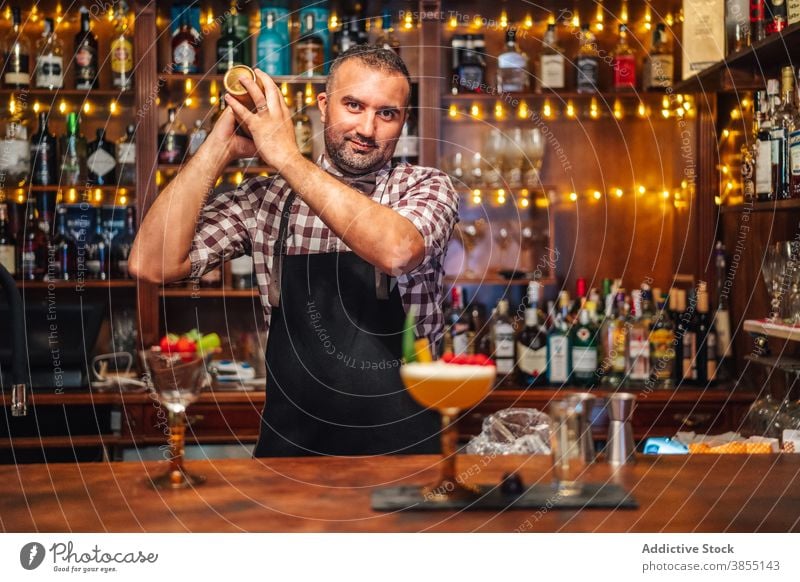 Fröhlicher Barmann, der einen Cocktail im Shaker mixt Mann Barkeeper schütteln mischen Glück Abfertigungsschalter Glas Arbeit männlich Lebensmitte reif Job