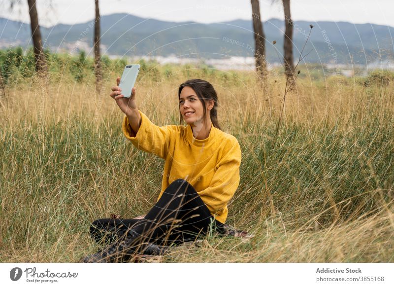 Lächelnde Frau nimmt Selfie in Wiese im Herbst sich[Akk] entspannen Smartphone Selbstportrait charmant Wochenende genießen Pullover gelb trocknen Feld Gerät