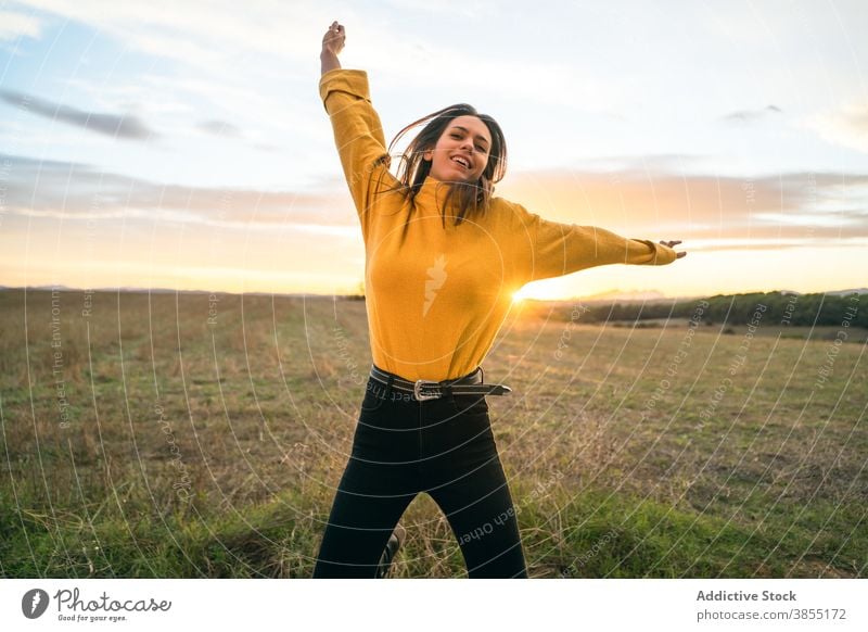 Fröhliche Frau springt im Feld bei Sonnenuntergang springen sorgenfrei Freiheit genießen Lächeln Moment Landschaft Outfit lässig Wiese ländlich Gegend aktiv