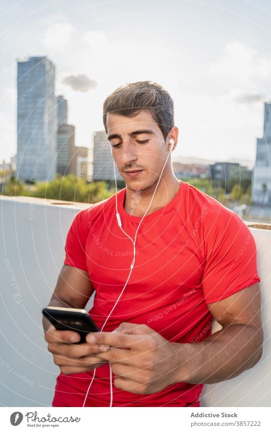 Sportlicher Mann mit Kopfhörern vor dem Training auf der Straße Sportler Smartphone vorbereiten urban zuhören jung muskulös Athlet Fitness Gerät Apparatur Musik