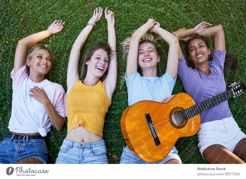 Glückliche multirassische Teenager mit Gitarre genießen Sommertag im Park Freundin Kälte Lügen heiter Zusammensein ruhen Frauen rassenübergreifend multiethnisch