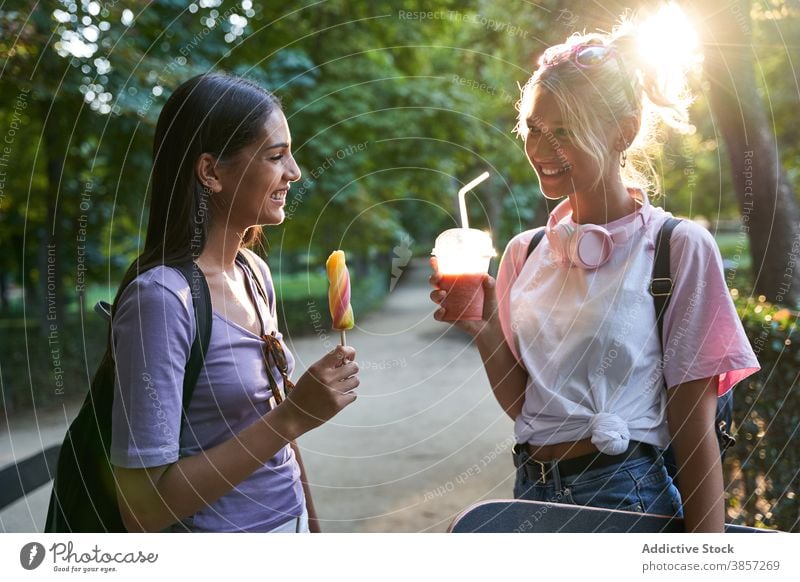 Glückliche Freundinnen mit Eis und Getränk haben Spaß im Park Sommer Speiseeis Stieleis trinken heiter Talkrunde Spaß haben Mädchen Zusammensein vielfältig