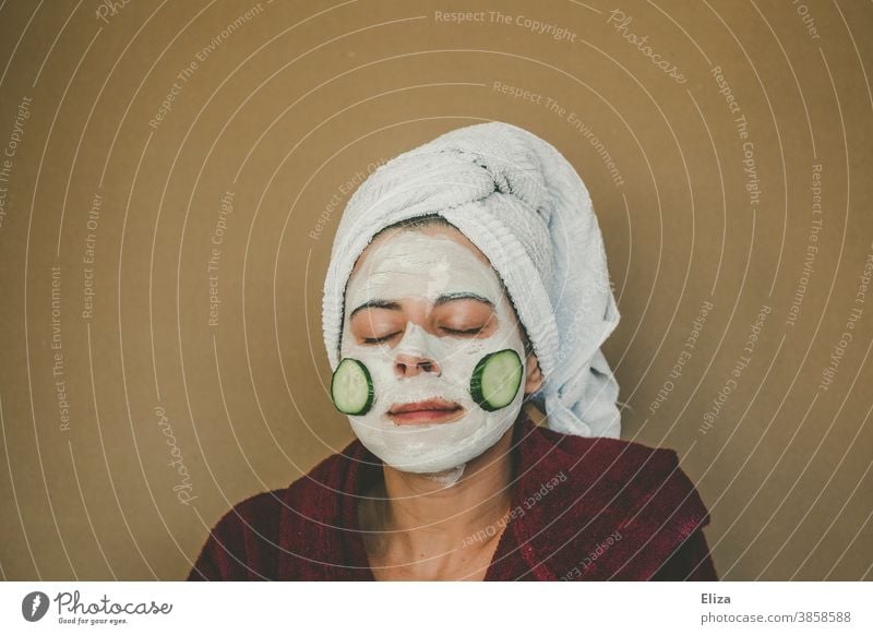 Eine Frau im Bademantel und mit Handtuchturban macht eine Gesichtsmaske und genießt diese mit geschlossenen Augen Kosmetik Haut Körperpflege Gesichtspflege