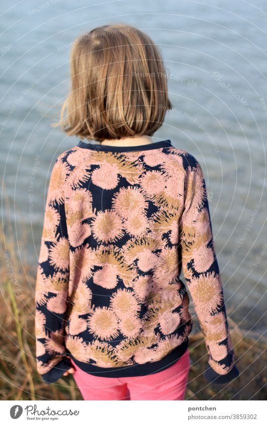 Mädchen steht am Ufer und blickt auf einen See. Rückansicht. Entspannung, Begeisterung, Neugierde. Kindheit mädchen ufer schilf neugierde natur pullover muster