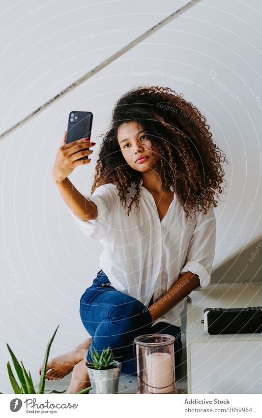 Stilvolle ethnische Frau nimmt Selfie zu Hause Smartphone Afro-Look krause Haare Telefon Fotografie modern jung schwarz Afroamerikaner Mobile Gerät Apparatur