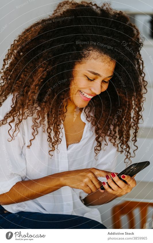 Stilvolle ethnische Frau verwendet Smartphone zu Hause Afro-Look krause Haare Telefon modern jung schwarz Afroamerikaner Mobile Gerät Apparatur Browsen
