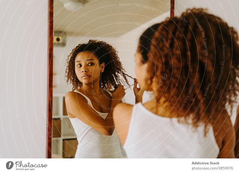 Junge ethnische Frau Anpassung Haar in der Nähe von Spiegel Behaarung Morgen zu Hause Afro-Look Frisur Routine Reflexion & Spiegelung Schönheit jung