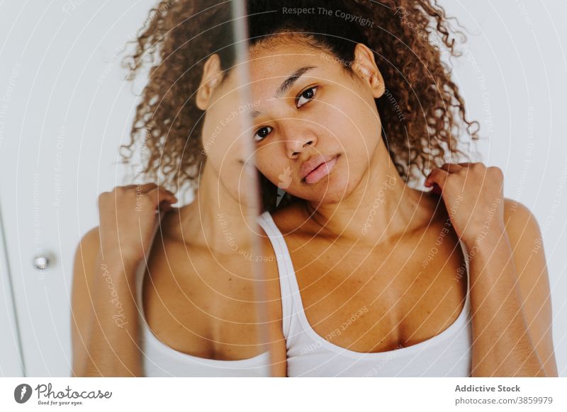 Entspannte ethnische Frau mit lockigem Haar steht in der Nähe von Spiegel zu Hause Windstille sich[Akk] entspannen Afro-Look krause Haare Morgen
