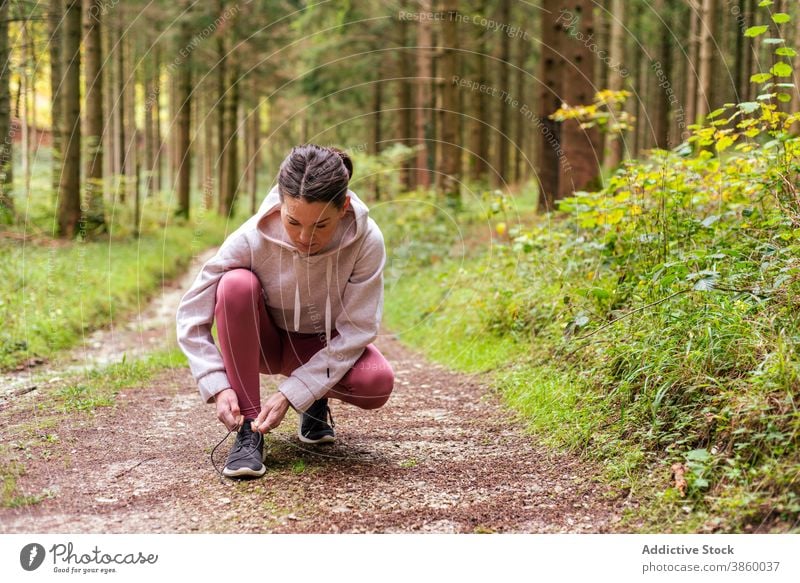 Sportliche Frau bindet Schnürsenkel im Wald Krawatte Schuhbänder Sportlerin Turnschuh Training Wälder Schuhe Athlet passen Sportkleidung Fitness Wellness Pause