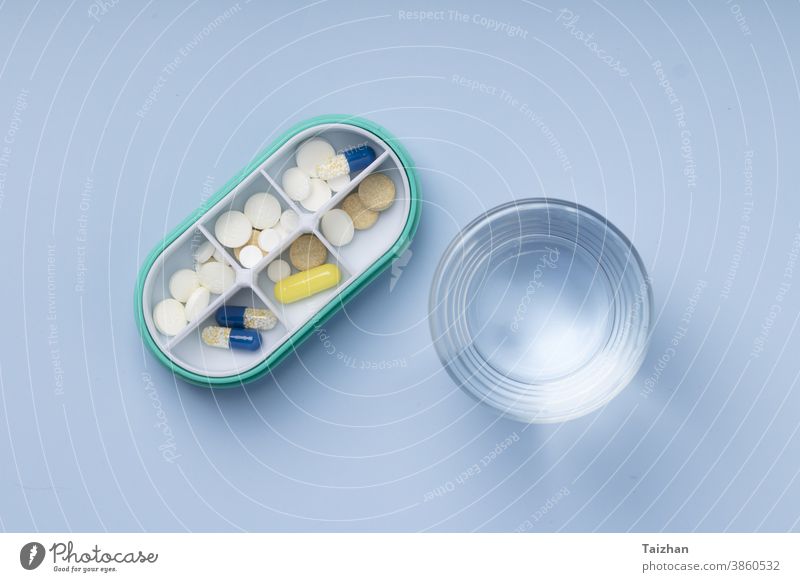Draufsicht auf Pillenbox und Wasserglas auf blauem Hintergrund Medizin Tag Organisator Gesundheitswesen Hinweis Erinnerung schreiben täglich Medikament offen