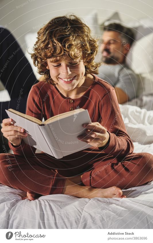 Nettes Kind liest Buch im Zimmer lesen Schlafzimmer clever unterhalten Vater Sohn Bett interessant heimwärts Etage Freude Literatur sitzen Komfort Zusammensein