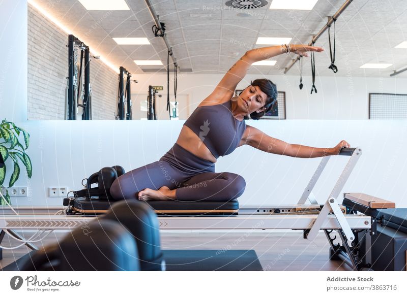 Fit Frau tun Seated Side Bend auf Pilates-Reformer Training Dehnung Übung sitzende Seitenkurve Fitnessstudio modern passen Maschine Körper schlank beweglich