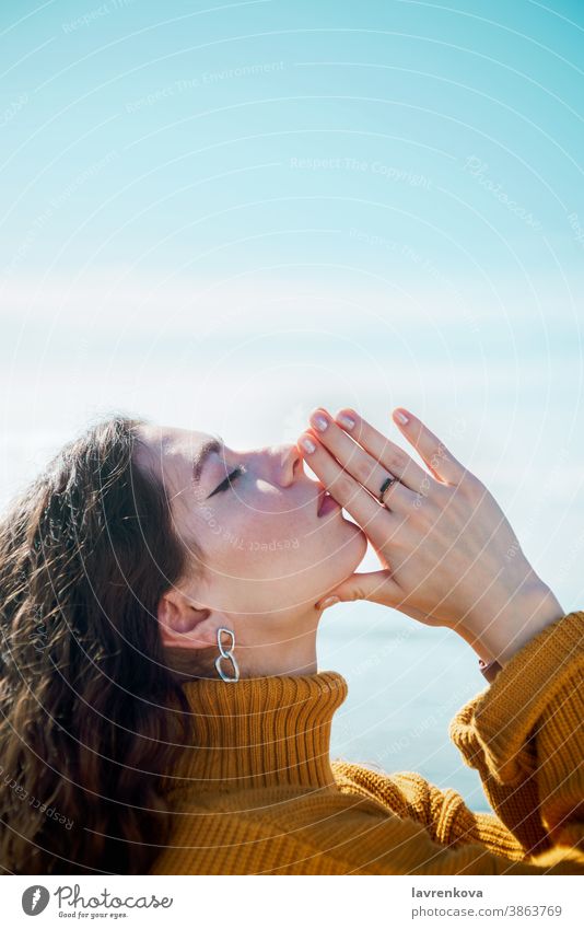 Profilporträt einer jungen erwachsenen weißen Frau mit geschlossenen Augen, die eine Namaste-Geste macht und ihre Hände vor dem blauen Himmel berührt Erholung