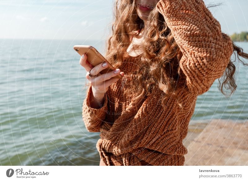 Nahaufnahme einer Frau, die ihr Telefon an einem Strand hält im Freien Beteiligung MEER Wasser Meer digital sozial Mobile Texten elektronisch Urlaub