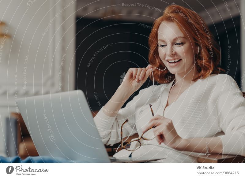 Zufriedener glücklicher Fuchs erfolgreiche Frau hat Videokonferenz, benutzt modernen Laptop-Computer und Kopfhörer, durchsucht Daten und arbeitet an Fernprojekt, posiert in moderner Wohnung, schaut Online-Webinar