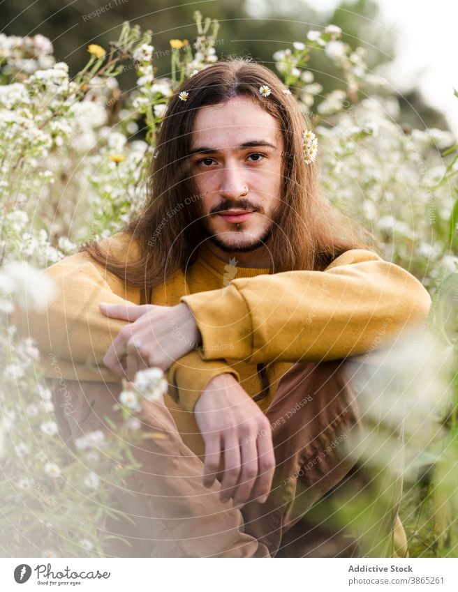 Junger Mann mit Blumen im langen Haar sitzt im Feld schwul romantisch lange Haare Blütezeit sich[Akk] entspannen ruhen Natur friedlich Windstille jung männlich