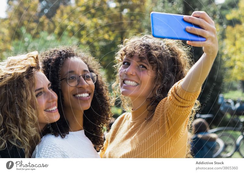 Fröhliche multiethnische Freunde nehmen Selfie im Park Frauen Zusammensein Freundschaft heiter Spaß haben freundlich Smartphone rassenübergreifend vielfältig