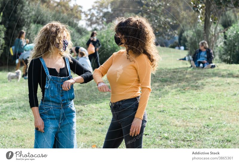 Frauen in Masken stoßen Ellbogen im Park Coronavirus Gruß Freund Zusammensein Bund 19 Mundschutz neue Normale Seuche gestikulieren Sicherheit Kommunizieren