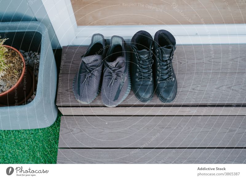 Männliches und weibliches Schuhwerk vor der Haustür Turnschuh Stiefel Schuhe Türschwelle Türöffnung Kabine Stil Mode Leder trendy hölzern Schritt Paar Objekt