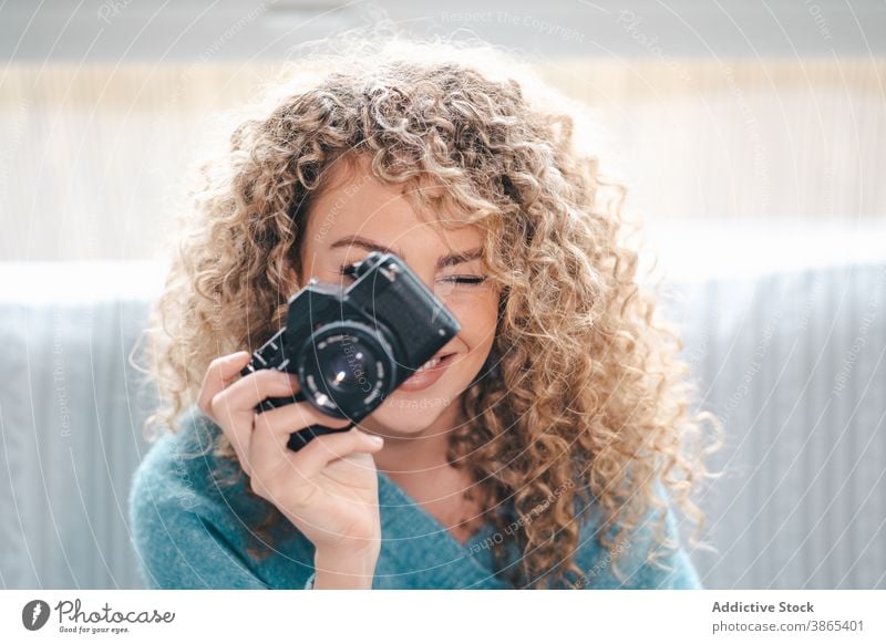 Fröhliche Frau mit Fotokamera zu Hause Fotograf fotografieren heiter heimwärts Talent gemütlich Fotoapparat Fotografie krause Haare hell Appartement lässig