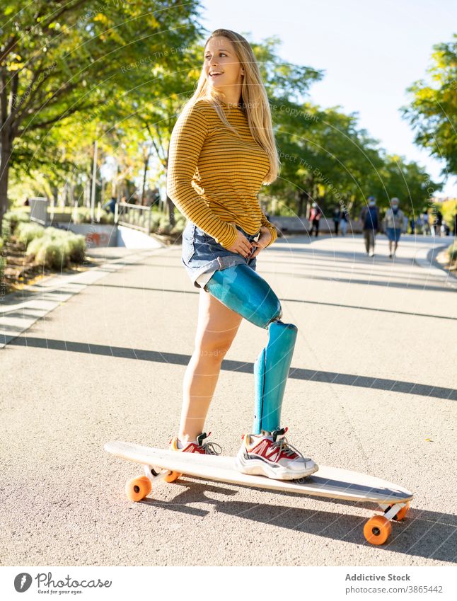Lächelnde Frau reitet Longboard in der Stadt Bionik Prothesen Mitfahrgelegenheit Skater Bein heiter deaktivieren künstliches Glied Amputierte Straße Glück urban