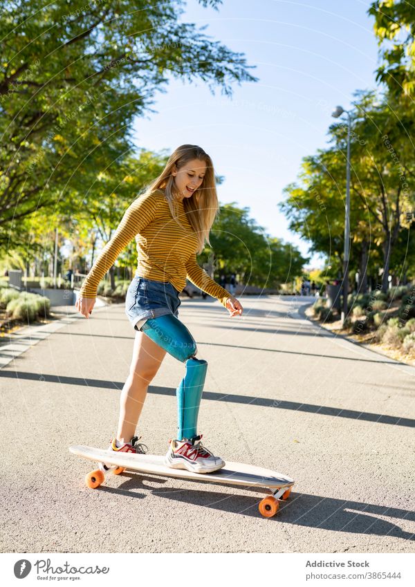 Lächelnde Frau reitet Longboard in der Stadt Bionik Prothesen Mitfahrgelegenheit Skater Bein heiter deaktivieren künstliches Glied Amputierte Straße Glück urban